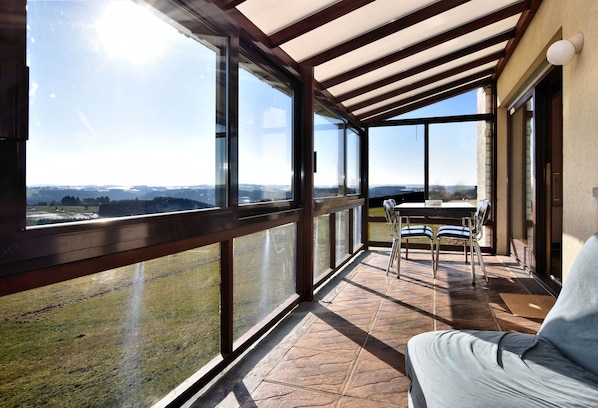 Un balcon avec une table et des chaises, de grandes fenêtres et une vue sur la campagne.