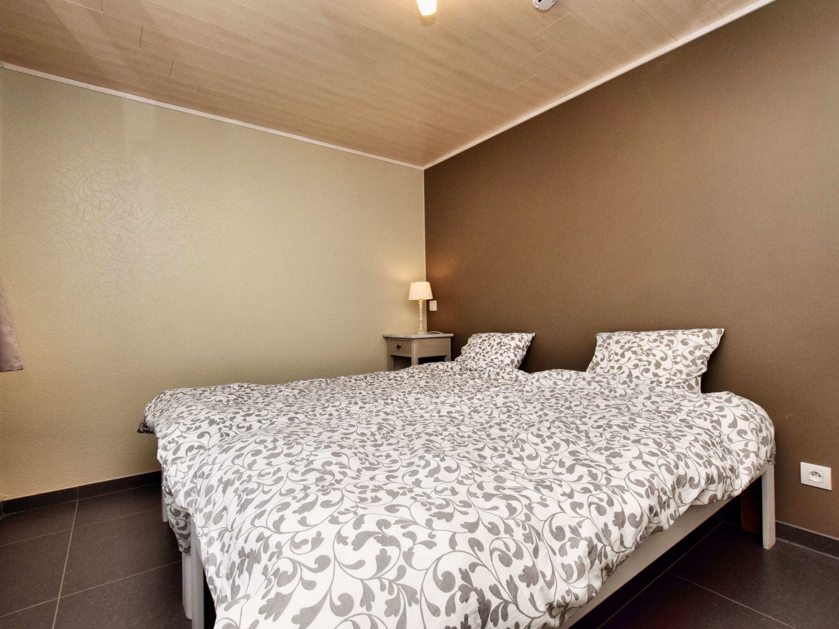 Een slaapkamer met een groot bed, een nachtkastje met een lamp en een stopcontact.