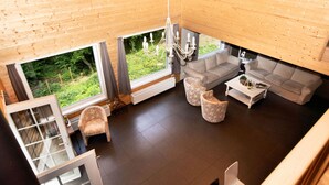 A modern living room with a sofa, two armchairs, a coffee table, and a chandelier. Large windows offer a view of a green garden. - Spacious Family Villa in Soy (Erezee)