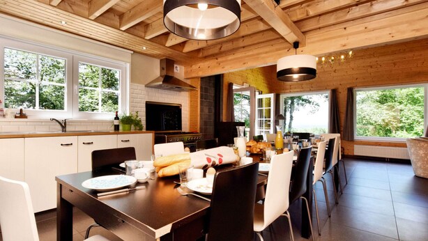 A modern kitchen with wooden beams, large windows, and a dining area with chairs and a table set for breakfast. - Spacious Family Villa in Soy (Erezee)