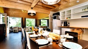 A modern kitchen with wooden beams, a dining table set for breakfast, and a view of the outdoors. - Spacious Family Villa in Soy (Erezee)