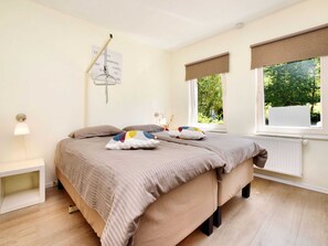 A bedroom with a bed, two windows with blinds, a bedside lamp, and a wall clock.