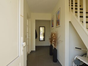 A hallway with a staircase on the right, a door on the left, and a mirror on the wall.