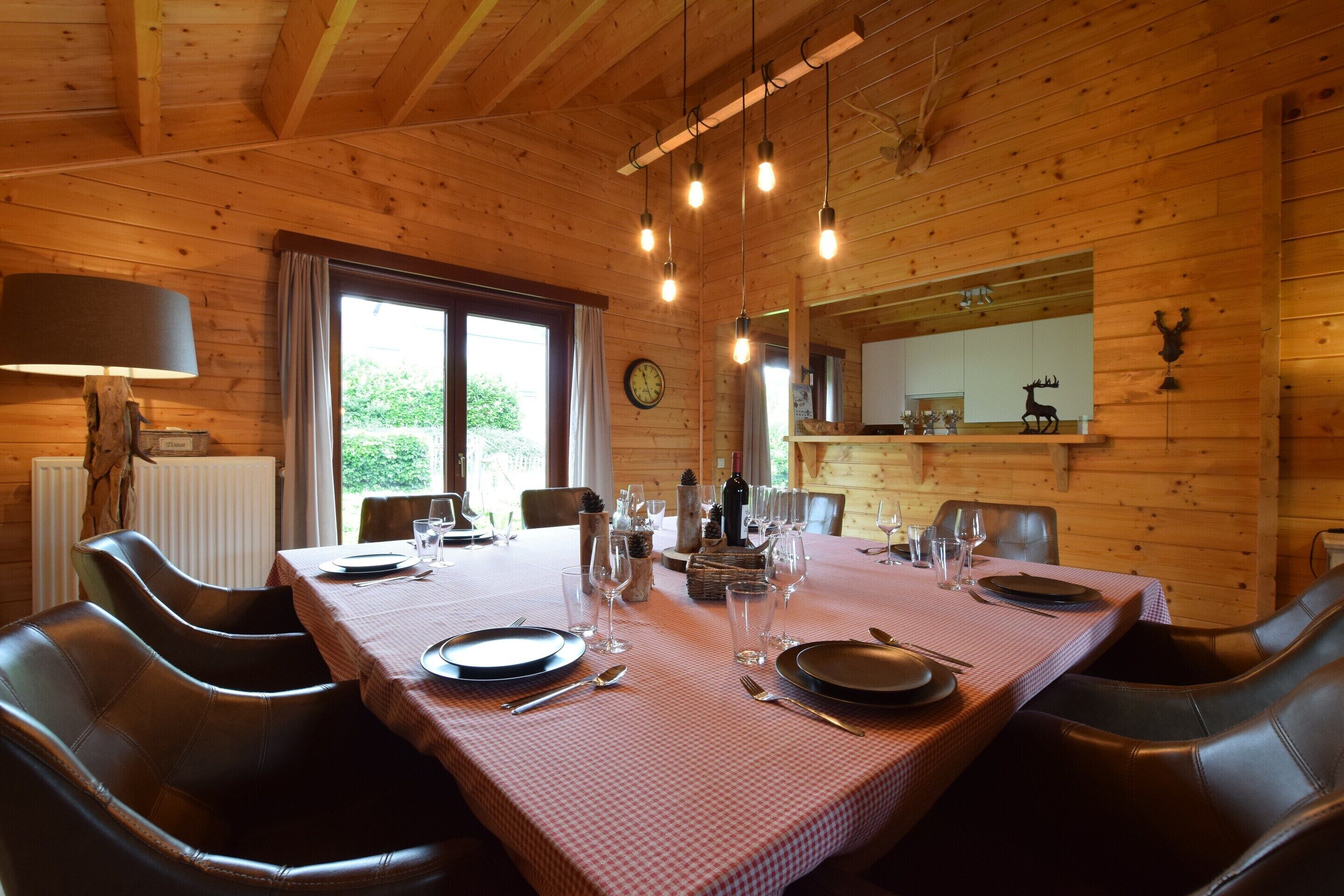 A wooden cabin dining room with a checkered tablecloth, leather chairs, and hanging light fixtures.