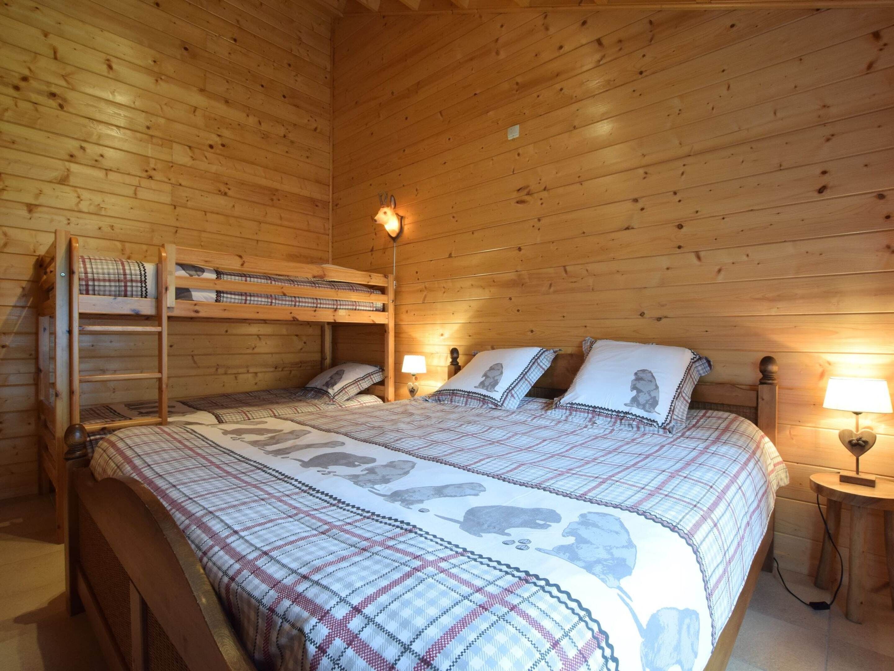 A wooden cabin room with a bunk bed, two bedside tables with lamps, and a bed with a patterned blanket.