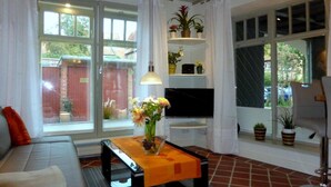 A living room with a sofa, a TV, a table with a vase of flowers, and a window with curtains. - Apartments gatehouse - old town (Lüneburg)
