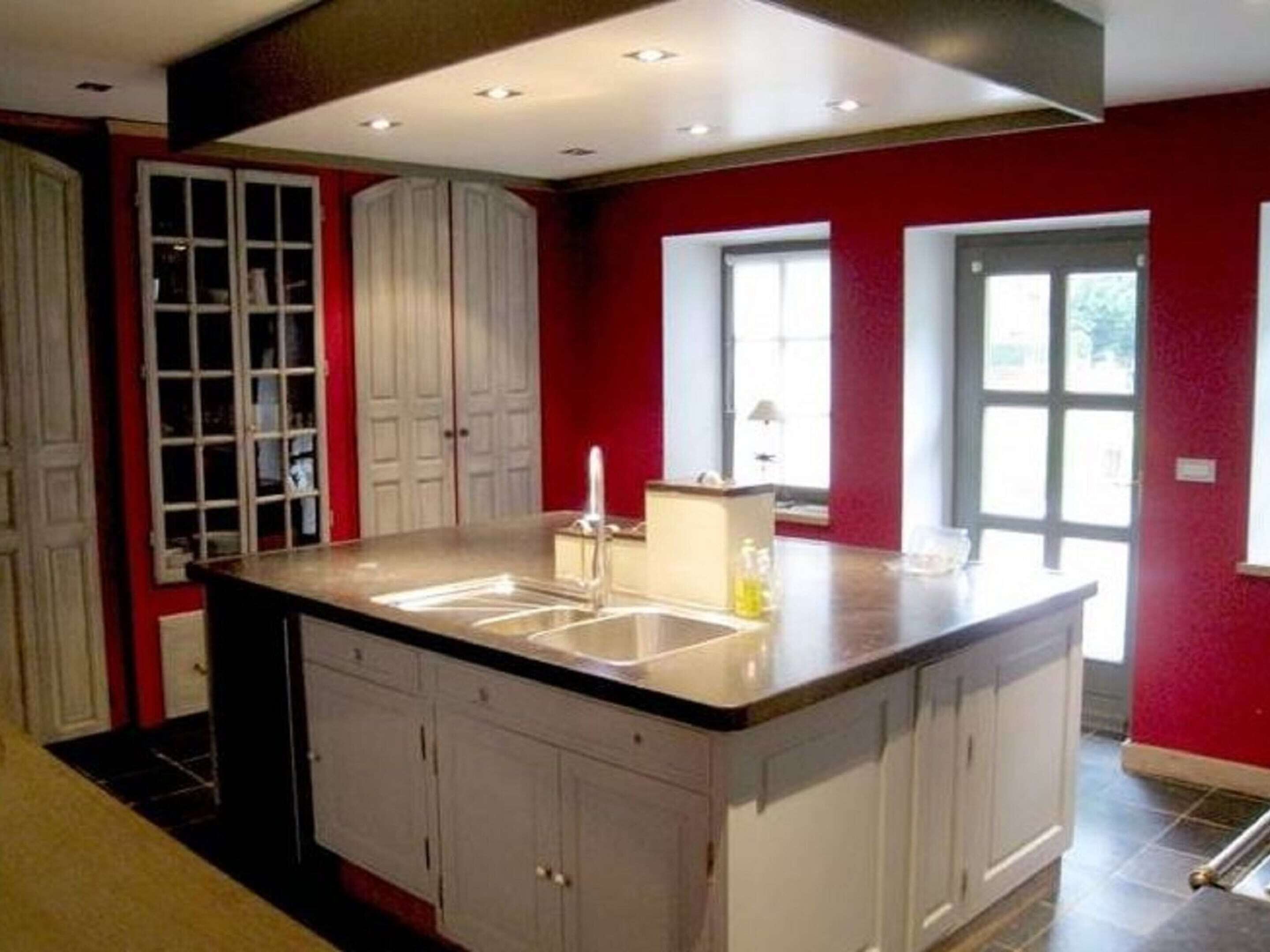 A kitchen with a central island, white cabinets, and red walls.