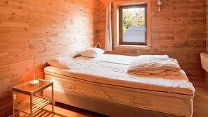 A wooden cabin bedroom with a large bed, a small window, and a wooden ceiling. - Villa in Freyneux With Garden (Manhay)