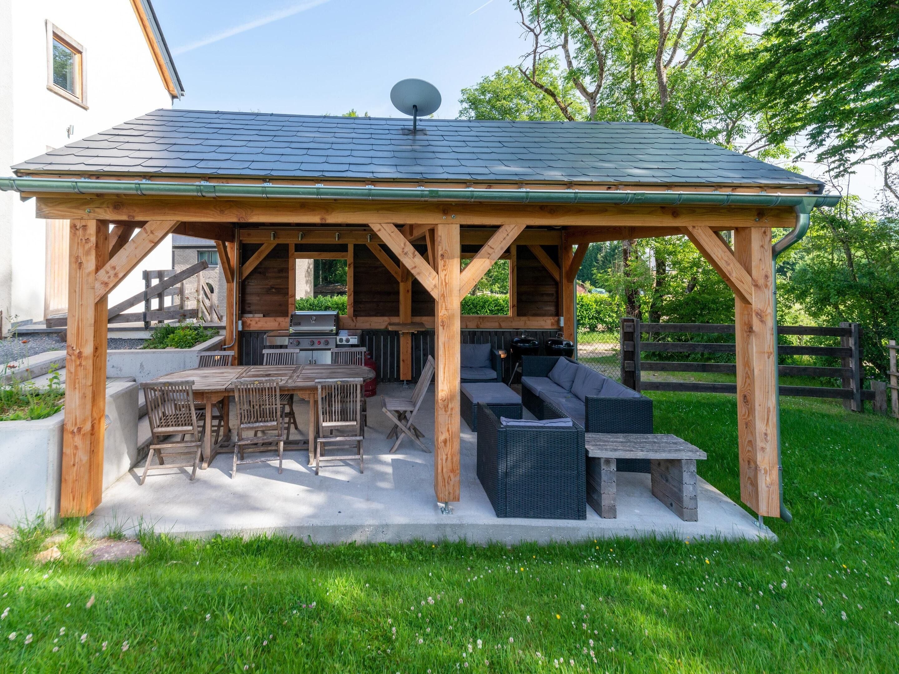 A wooden gazebo with a grill, seating, and a satellite dish.