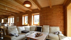 A cozy living area with a beige leather sofa, a wooden coffee table, and a dining area with a wooden table and chairs. - Villa in Freyneux With Garden (Manhay)