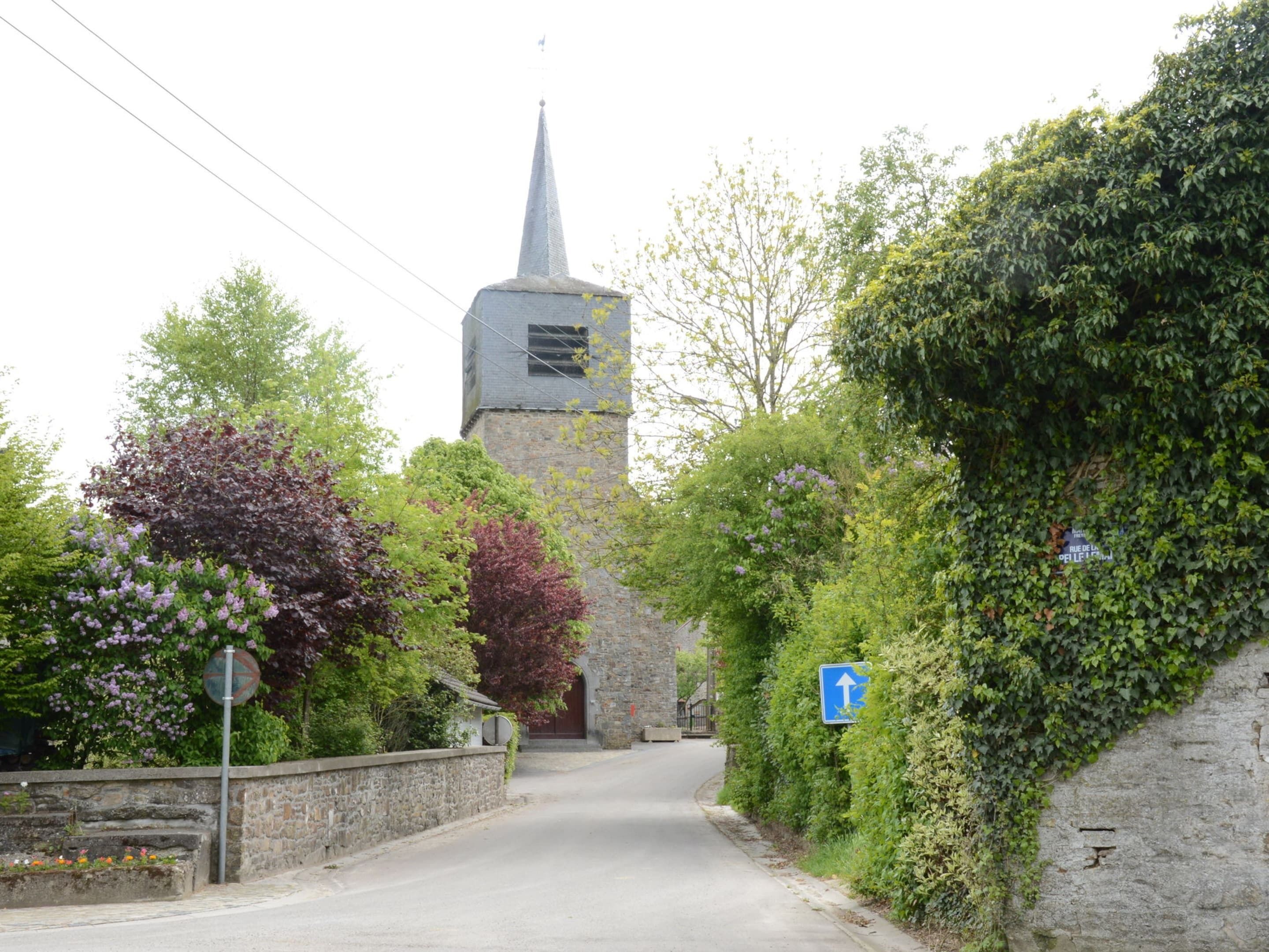 A narrow street with a church tower and a blue directional sign.