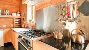 A modern kitchen with wooden cabinetry, stainless steel appliances, and a variety of utensils hanging on the wall. - Villa in Freyneux With Garden (Manhay)