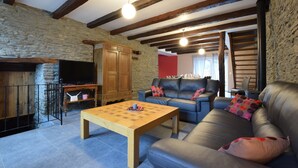Un salon chaleureux avec un mur en pierre, des poutres apparentes, un canapé et un téléviseur.