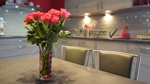 Une cuisine moderne aux murs rouges, une table à manger agrémentée d’un vase de roses roses et un îlot de cuisine doté d’un évier et d’un plan de travail.