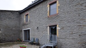 Un bâtiment en pierre doté d’un petit espace extérieur aménagé avec des sièges, un pot de fleurs et un escalier menant à un niveau supérieur.