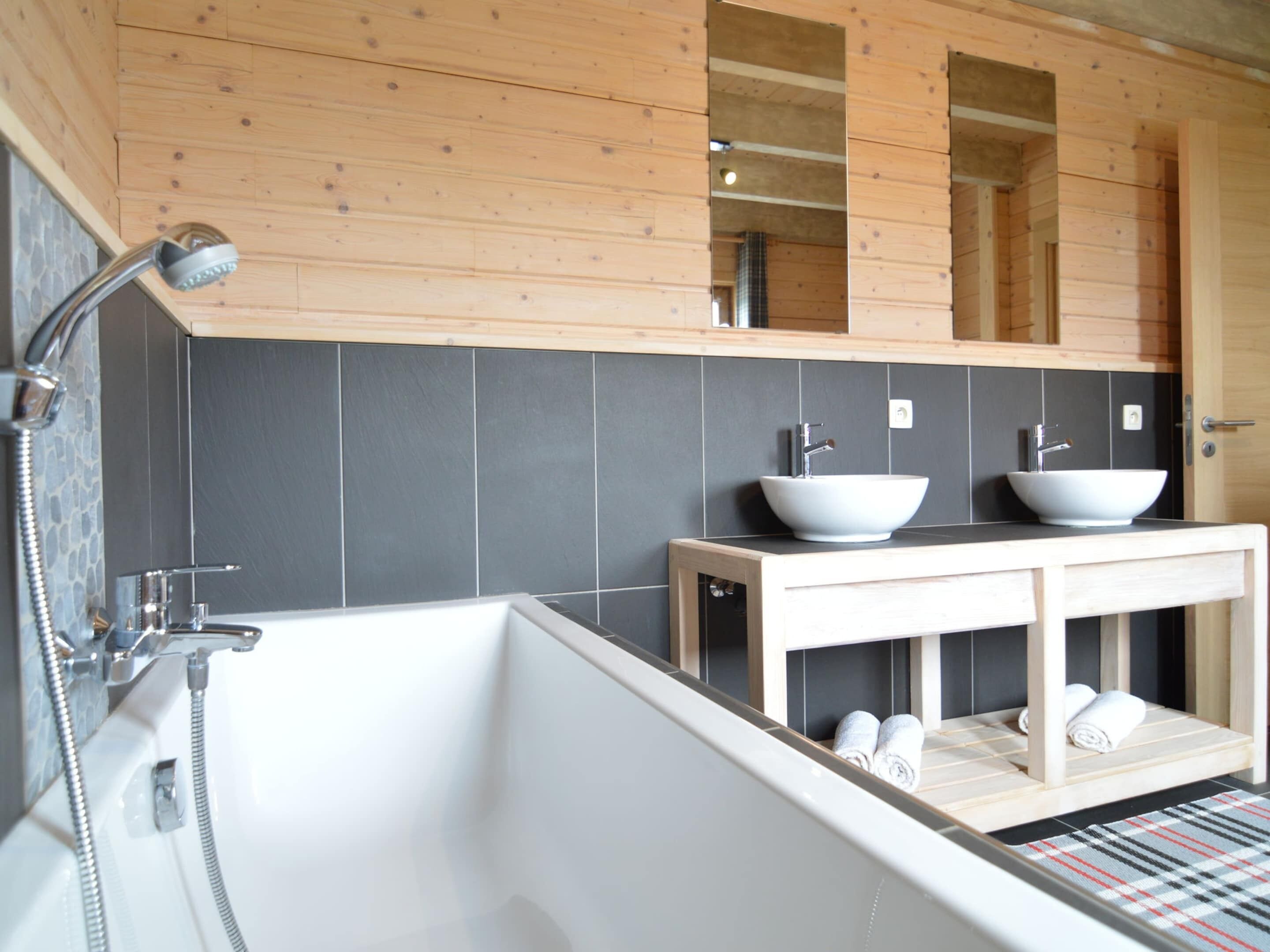 A modern bathroom with a freestanding bathtub, two vessel sinks, and a wooden vanity.