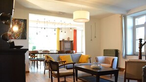 Una sala de estar acogedora con una mesa de centro de madera, un sofá y sillas. Se observa un comedor con sillas y una mesa al fondo.