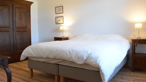 Un dormitorio con una cama grande, un armario de madera, dos mesitas de noche con lámparas y un candelabro en el techo.