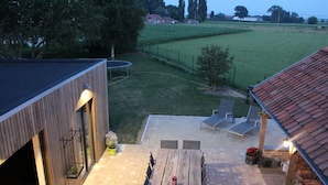 A modern outdoor patio with a wooden deck, a trampoline, and a seating area with lounge chairs. - Wonderful Country House With Huge Garden (Poperinge)