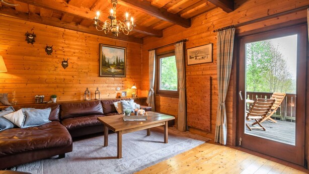 A cozy cabin interior with a wooden ceiling, a chandelier, a large window with curtains, a wooden sofa, and a dining table. - Very Spacious, Detached Holiday Home in Carinthia near Skiing & Lakes (Gnesau)