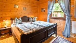 A wooden cabin bedroom with a double bed, a chandelier, a nightstand, and a window with curtains. - Very Spacious, Detached Holiday Home in Carinthia near Skiing & Lakes (Gnesau)