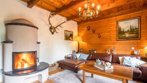 A cozy room with a fireplace, wooden ceiling, leather sofa, and a chandelier. - Very Spacious, Detached Holiday Home in Carinthia near Skiing & Lakes (Gnesau)