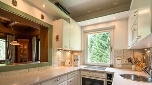 A modern kitchen with white cabinets, a built-in oven, a stovetop, and a window with a view of trees. - Very Spacious, Detached Holiday Home in Carinthia near Skiing & Lakes (Gnesau)