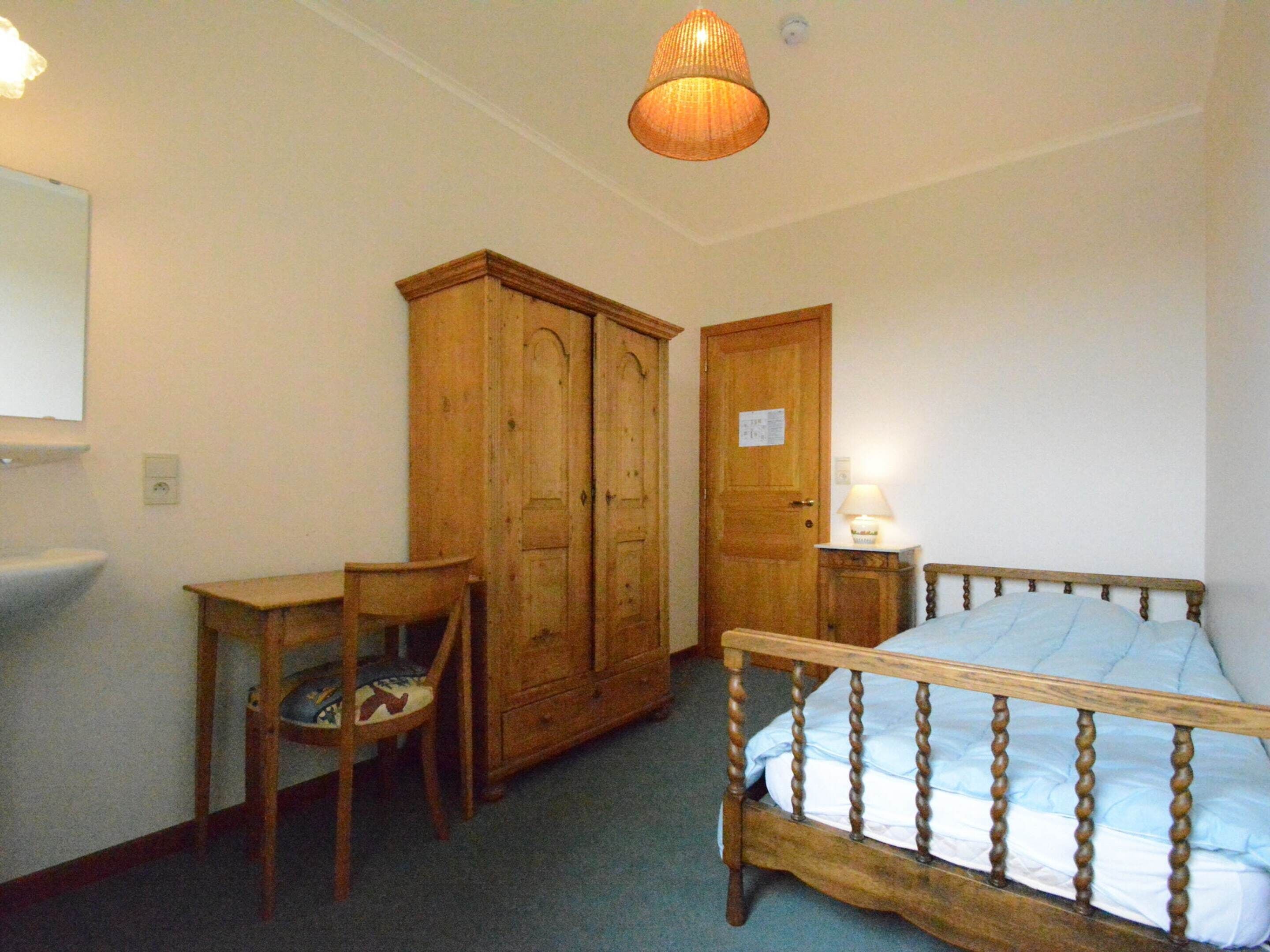 Ein Schlafzimmer mit einem hölzernen Bett, einem Schrank, einem Schreibtisch und einem Stuhl.