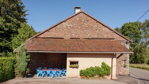 A stone building with a tiled roof, a gravel driveway, and a table with blue chairs outside. - Farmhouse in Basse-bodeux Near Forest (Trois-Ponts)