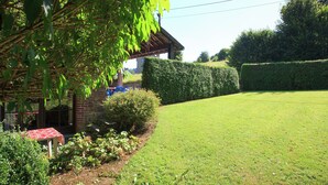 A garden with a brick building, a red table, and a neatly trimmed hedge. - Farmhouse in Basse-bodeux Near Forest (Trois-Ponts)