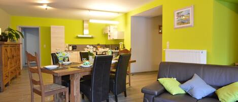 A modern living room with a brown leather sofa, a dining table set for four, and a kitchen in the background.