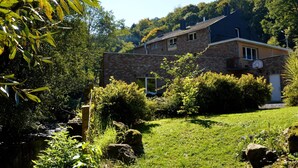 A two-story house with a brick exterior, surrounded by lush greenery and a small stream. - Cozy Holiday Home in Theux (Theux)
