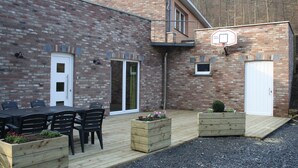 A brick building with a basketball hoop, a wooden deck, and outdoor seating. - Cozy Holiday Home in Theux (Theux)