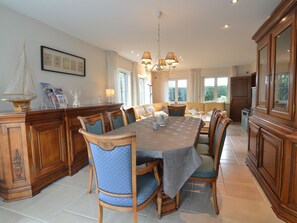 A spacious dining area with a large wooden table, upholstered chairs, and a chandelier.