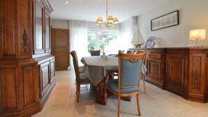 Een eetruimte met een ronde tafel, stoelen, houten kasten en een kroonluchter.