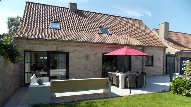 Een huis met pannendak, een terras met tuinmeubilair en een groot raam.