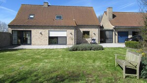 Een tweelaags huis met een pannendak, een garage en een kleine tuin met een bankje.