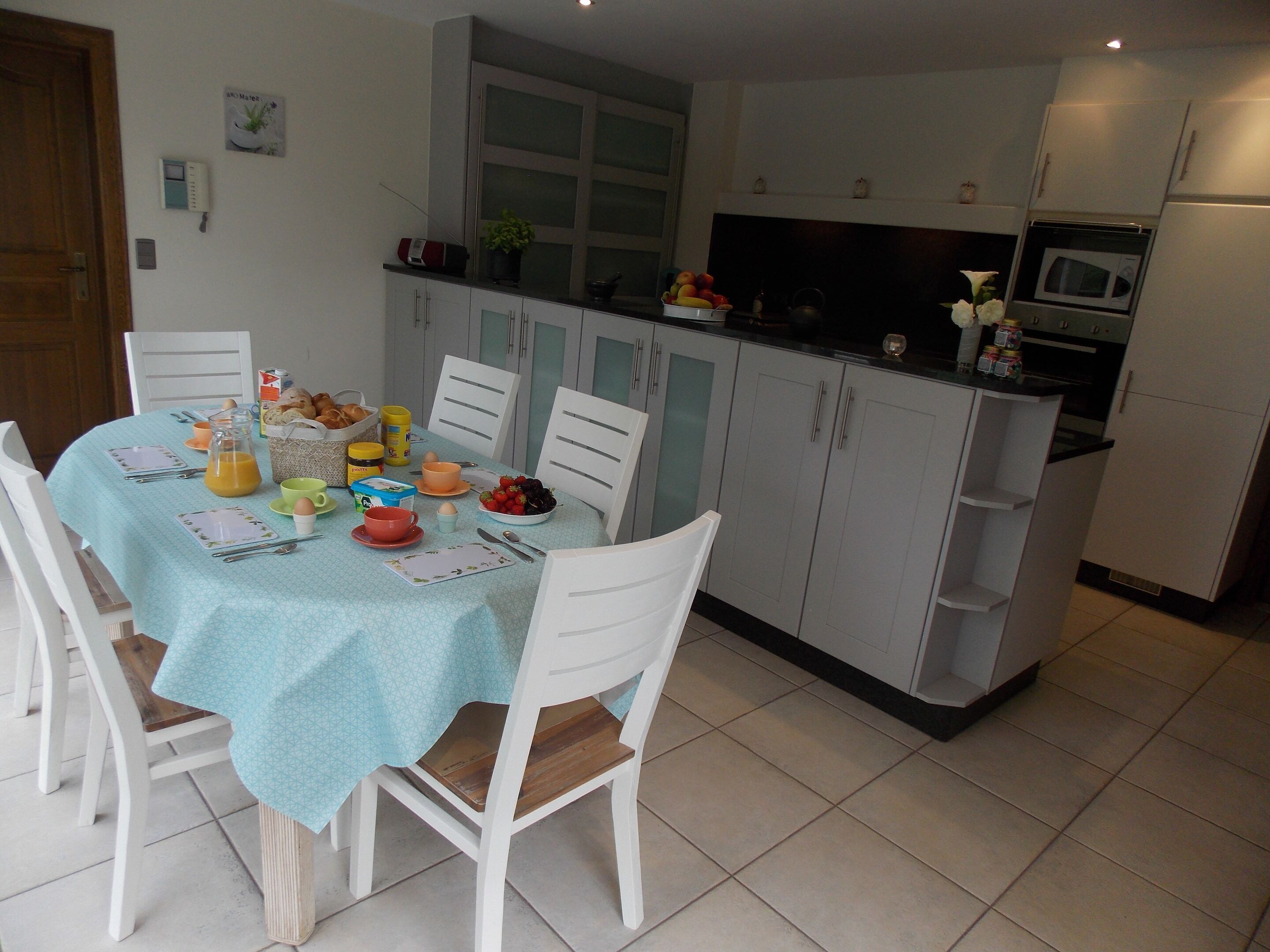 A kitchen with a dining table set for breakfast, white cabinets, and a microwave.