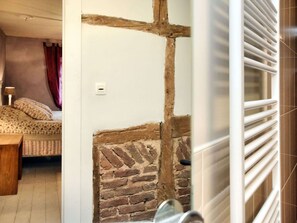 Une pièce avec un mur en briques, une poutre en bois, un lit avec une literie à motifs et un radiateur blanc.