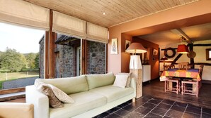 A cozy living area with a light green sofa, a dining table with wooden chairs, and a stone wall. - Holiday Home in Vielsalm (Vielsalm)