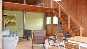 A cozy cabin interior with a wooden staircase, a sofa, a chair, and a table.