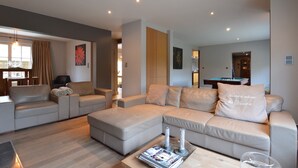 Een moderne woonkamer met een modulaire bank, een salontafel met tijdschriften en een pooltafel op de achtergrond.