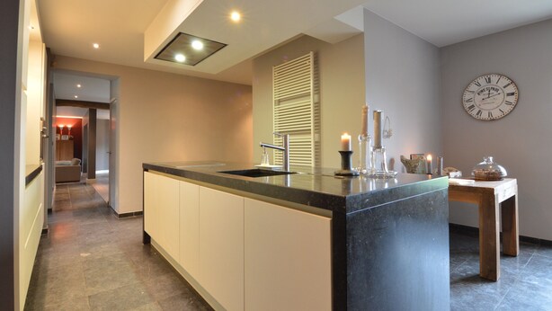 Een moderne keuken met een centraal eiland, een inbouwoven en een wandklok.