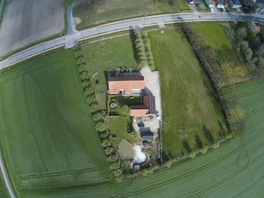 Vue aérienne d’une propriété comprenant un bâtiment principal, une allée et des champs verdoyants environnants.