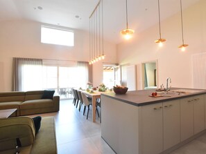 A modern kitchen with a central island, dining area with chairs, a sofa, and a large window providing natural light. - Tasteful Holiday Home in Sijsele-brugge With Garden (Damme)