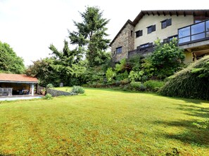Un vaste jardin à l’arrière de la maison, avec une piscine, un patio couvert et un bâtiment en pierre doté de grandes fenêtres.