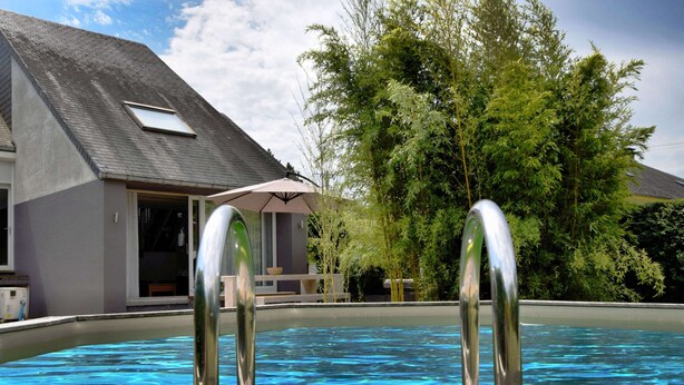 Piscina com grades de metal, cercada por uma casa e vegetação.