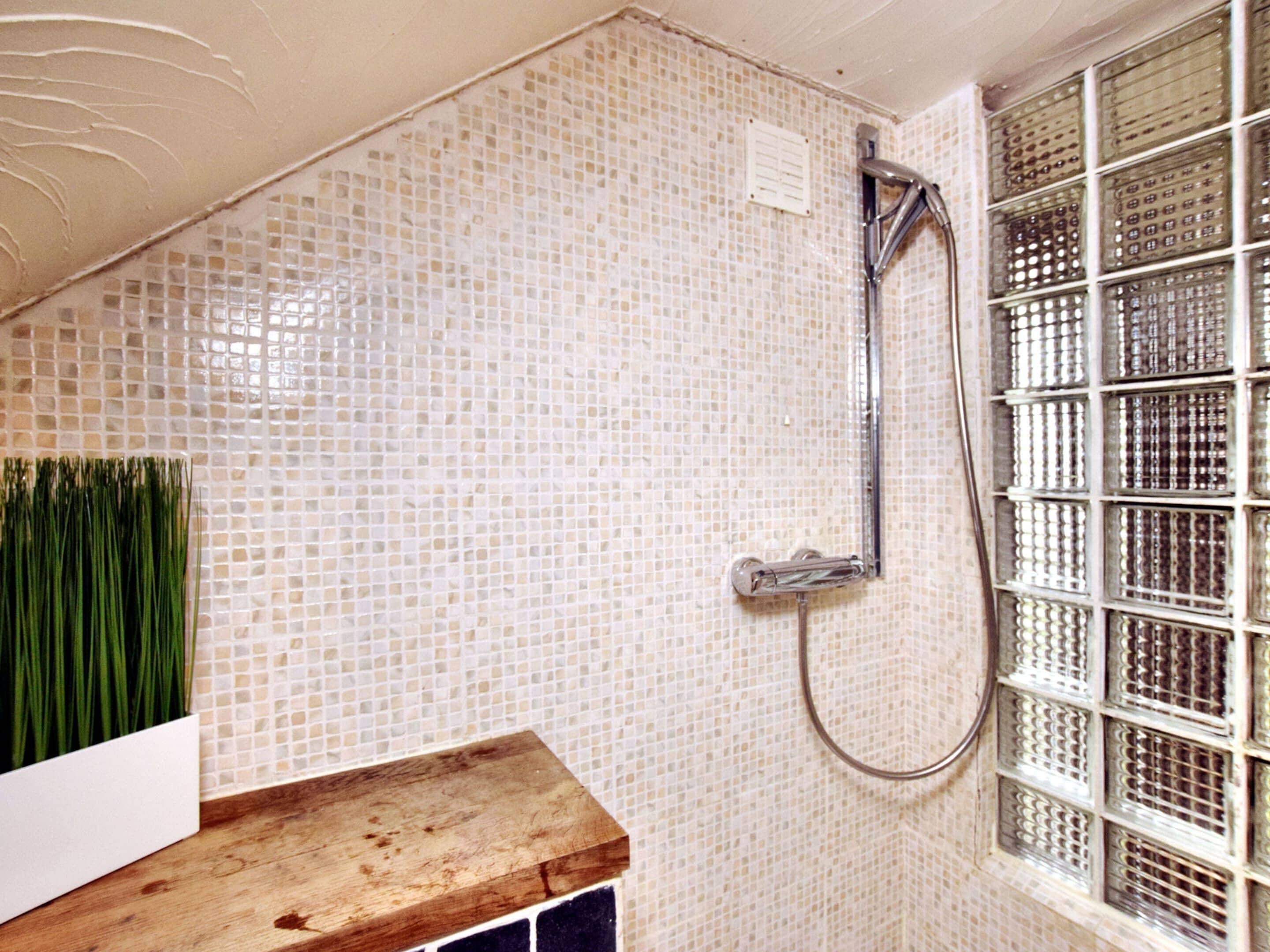 Ein Badezimmer mit Mosaikfliesen, einer Holzauslage und einer Dusche mit einem Metallrost.