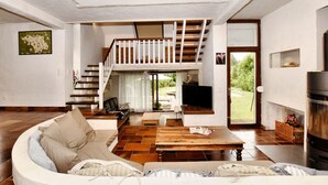 Uma sala de estar ampla com pé direito alto, escada de madeira, sofá, mesa de centro e lareira.