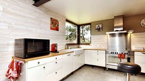 Uma cozinha moderna com armários brancos, um micro-ondas preto, fogão de aço inoxidável e uma janela que proporciona iluminação natural.